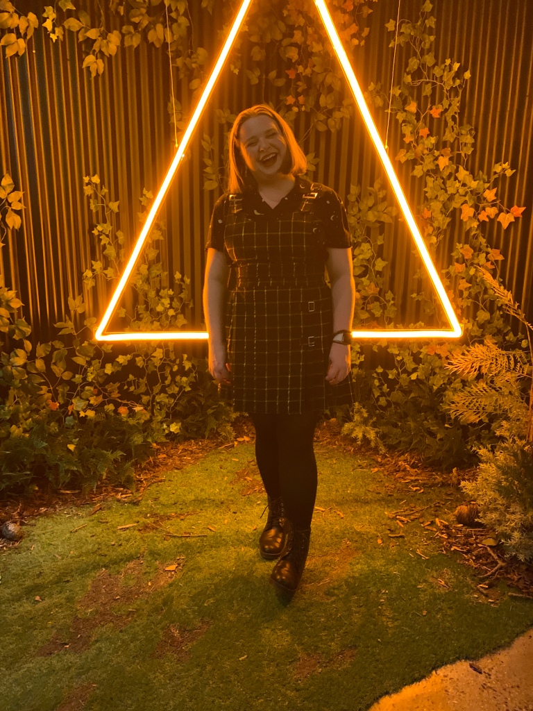 Carla Di Maggio laughing in front of vines, and a lit up triangle.